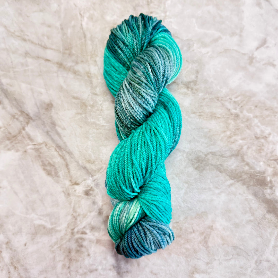 Turquoise and green skein of yarn on a textured beige background
